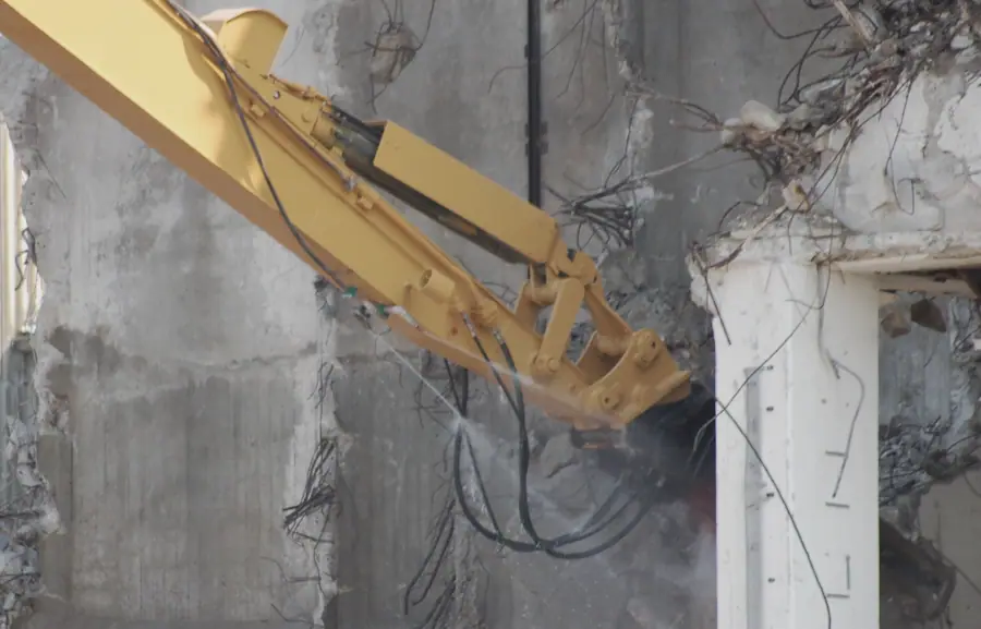 Demolition shear on a long-front excavator cutting through a concrete wall